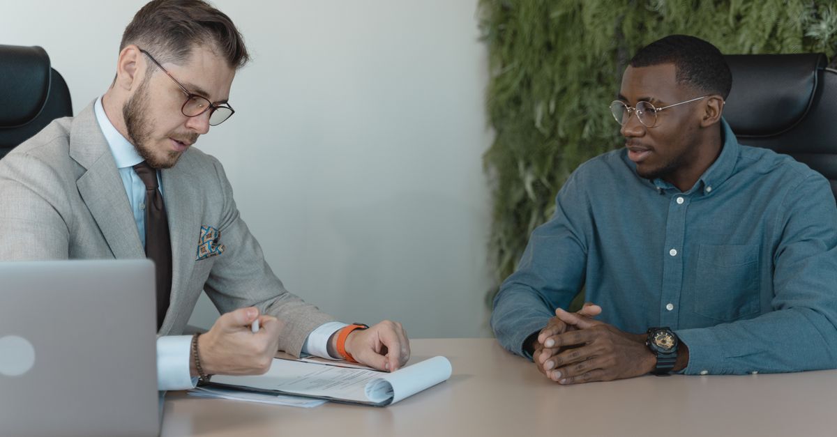 A licensed agent talking with an upline recruiter across a table in a modern office