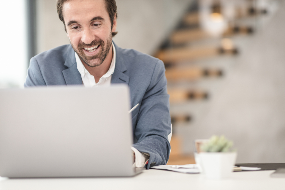 A smiling professional in a blazer working at a laptop in a bright modern office