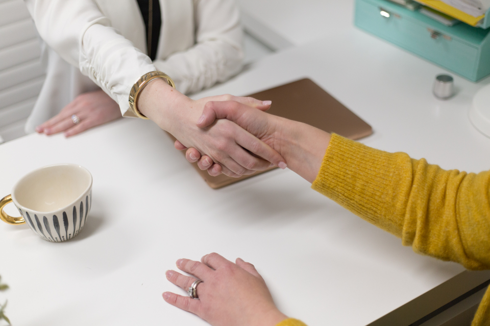 Two people shaking hands across a bright desk after an agent joins a new upline